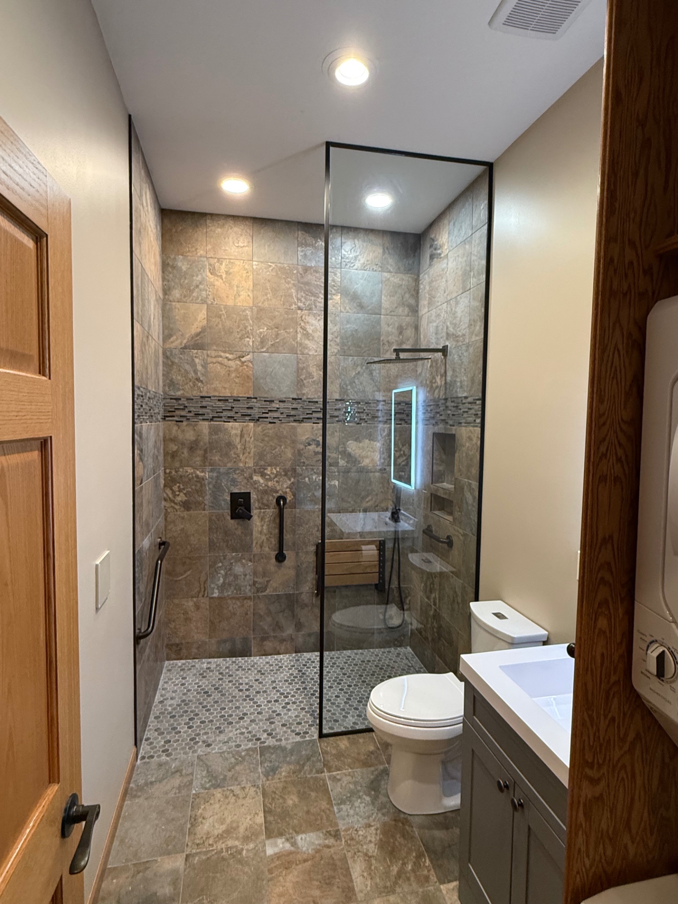 Walk-in shower with a fixed glass panel and slim black frame in a stone tiled bathroom