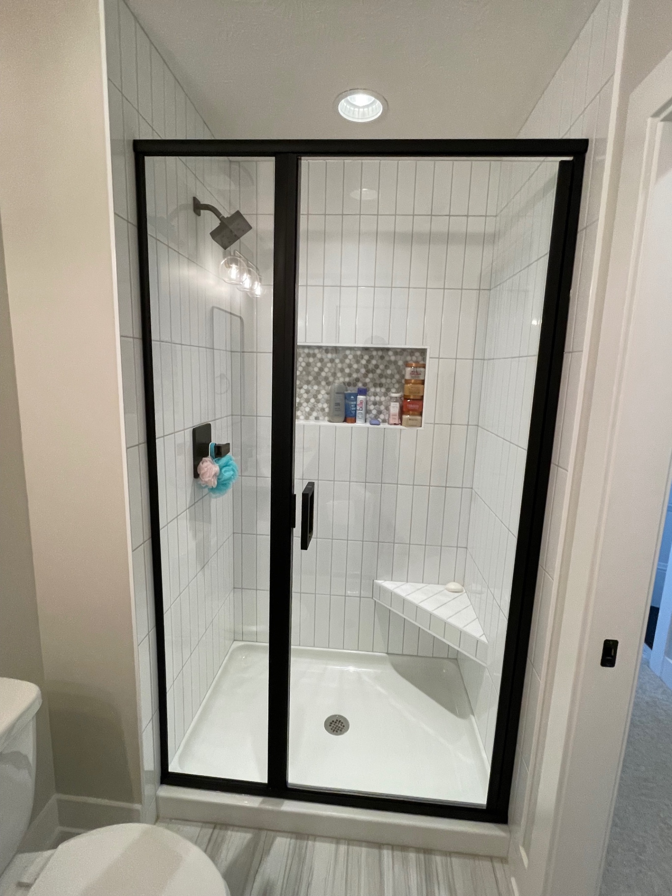 Framed shower door and inline panel with black frame and clear glass in a white tiled Omaha shower