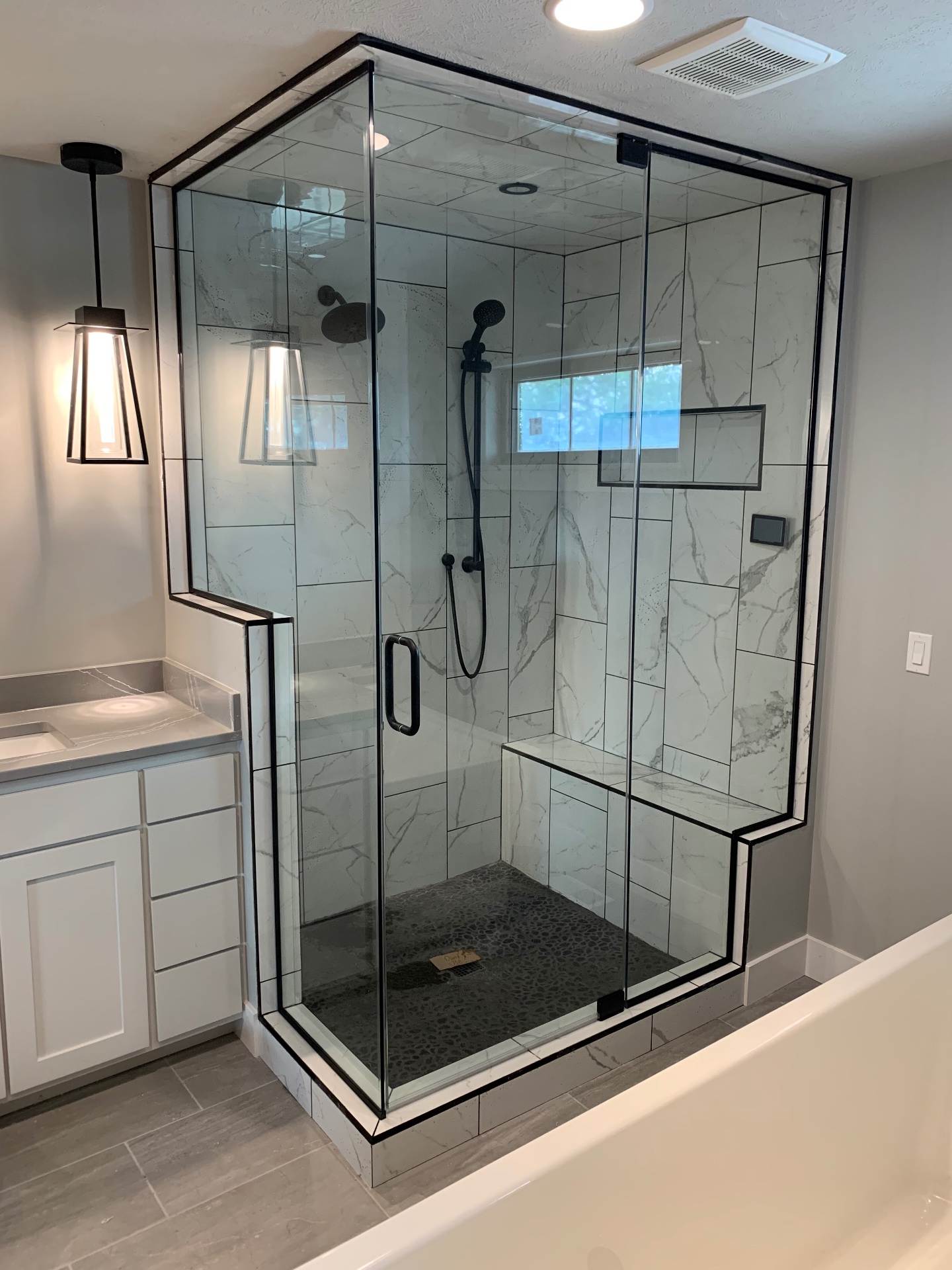 Black-framed shower enclosure with a swing door, fixed panels and a tiled bench in a marble-look shower