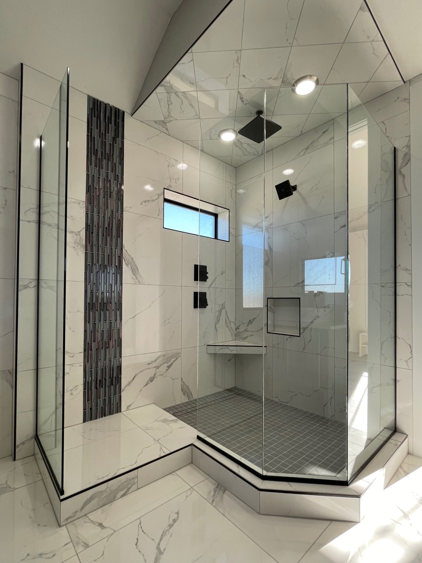 Frameless neo-angle shower enclosure in a marble tiled Omaha bathroom with a built-in bench