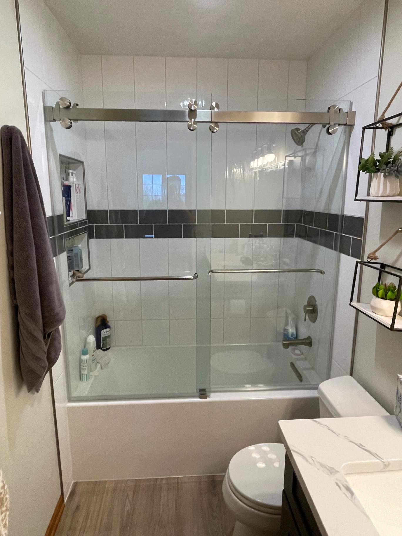 Frameless sliding tub enclosure with brushed nickel track and towel bar handles over a white bathtub