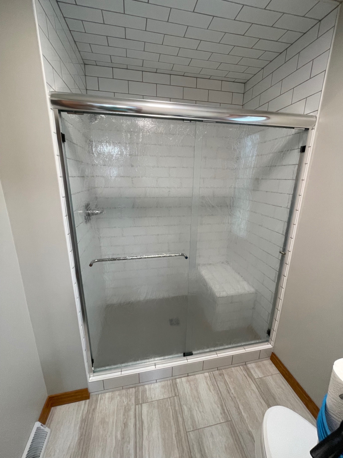 Semi-frameless bypass shower doors with rain textured glass and a brushed metal header in a subway tiled shower