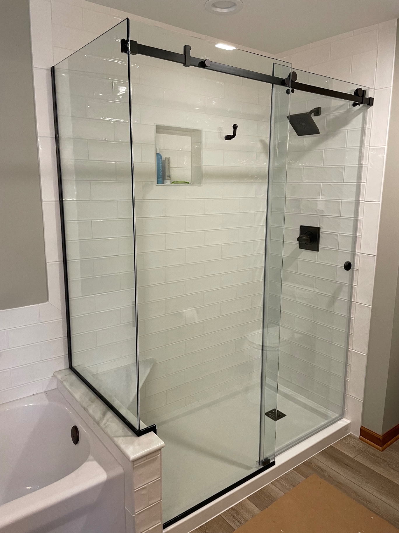 Frameless sliding shower door on a black top-mounted track with a return panel next to a bathtub