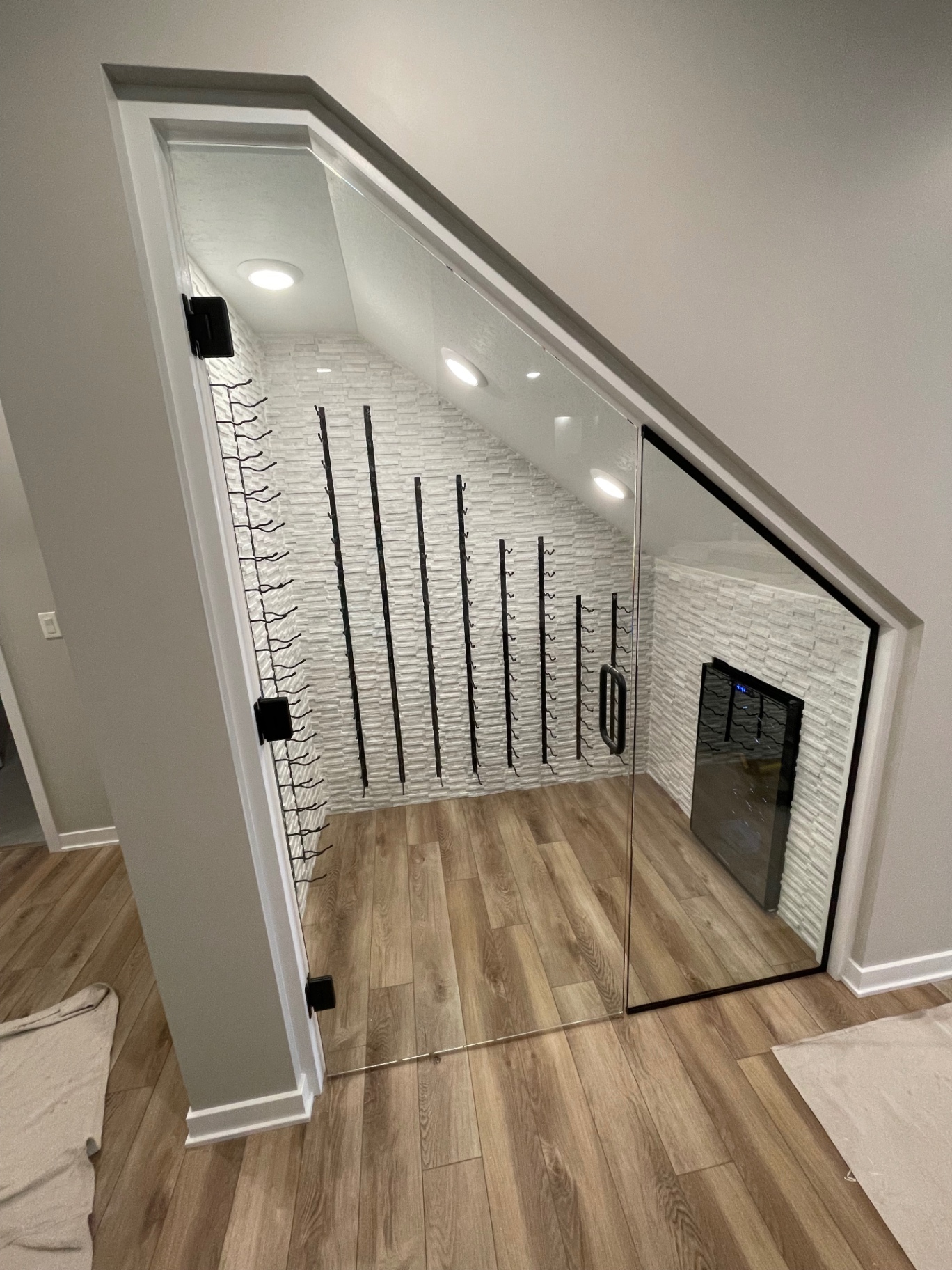 Custom angled glass wine room door and sidelite fitted under a staircase with black hardware