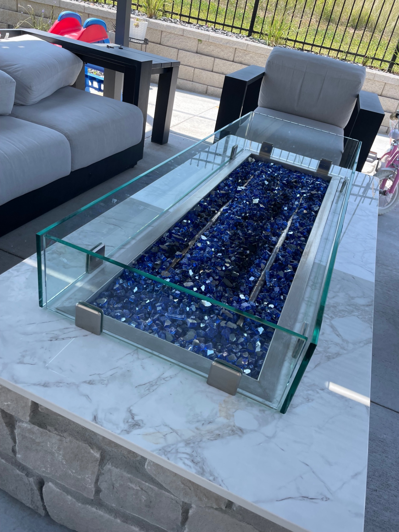 Custom clear glass wind guard panels fitted around an outdoor fire table on a marble patio table