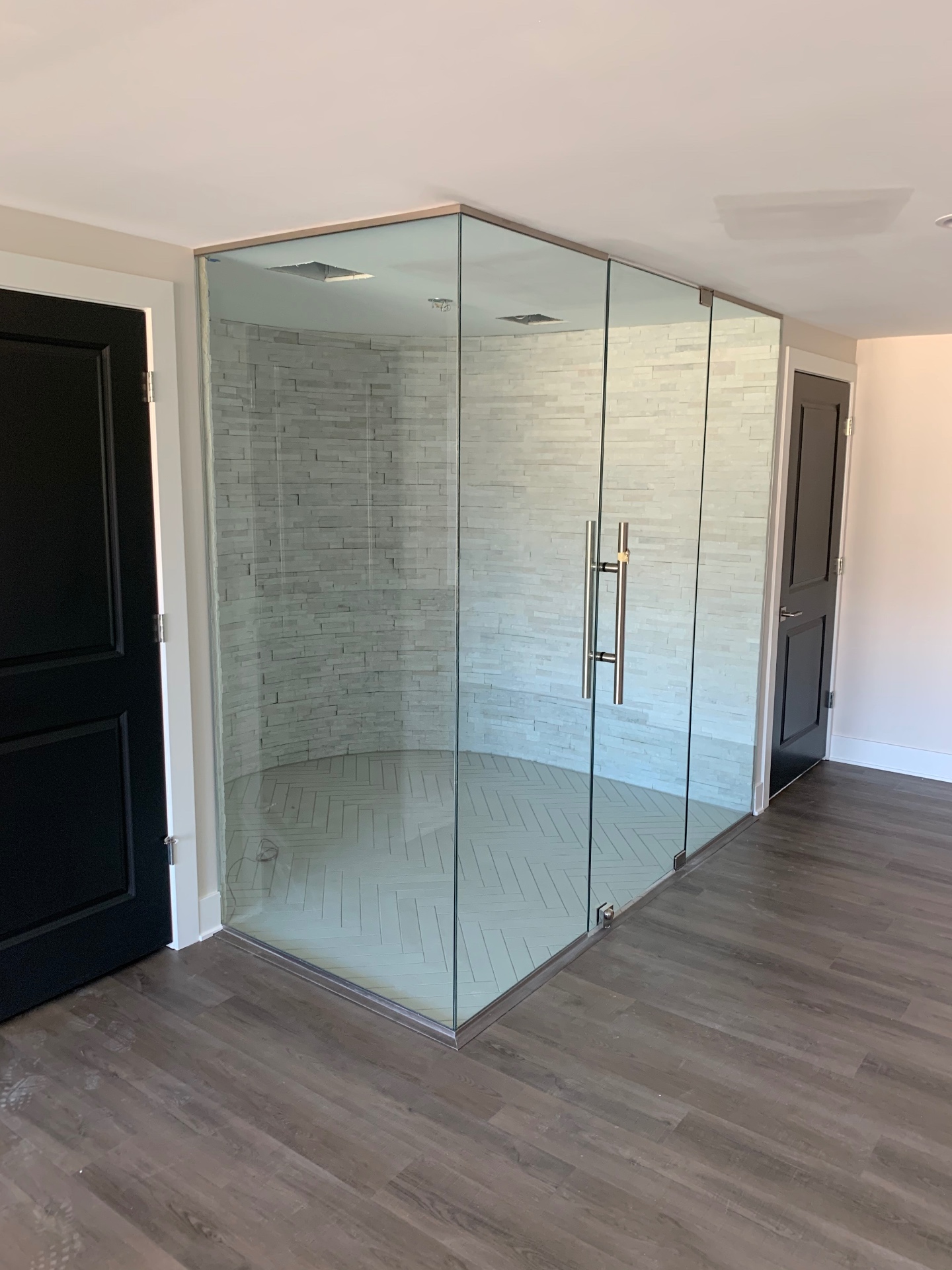 Floor-to-ceiling frameless glass shower enclosure with a ladder pull handle and stacked stone walls
